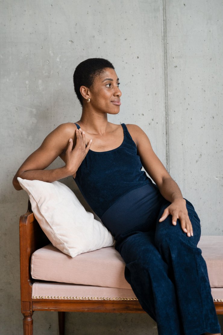 Model sitzt mit dem dunkelblauen Body und der Fiona Hose auf dem Tagesbett und blickt in Richtung des Fensters