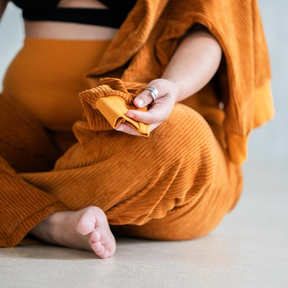 Model sitzt im ockerfarbigen Pyjama auf dem Boden im Schneidersitz.