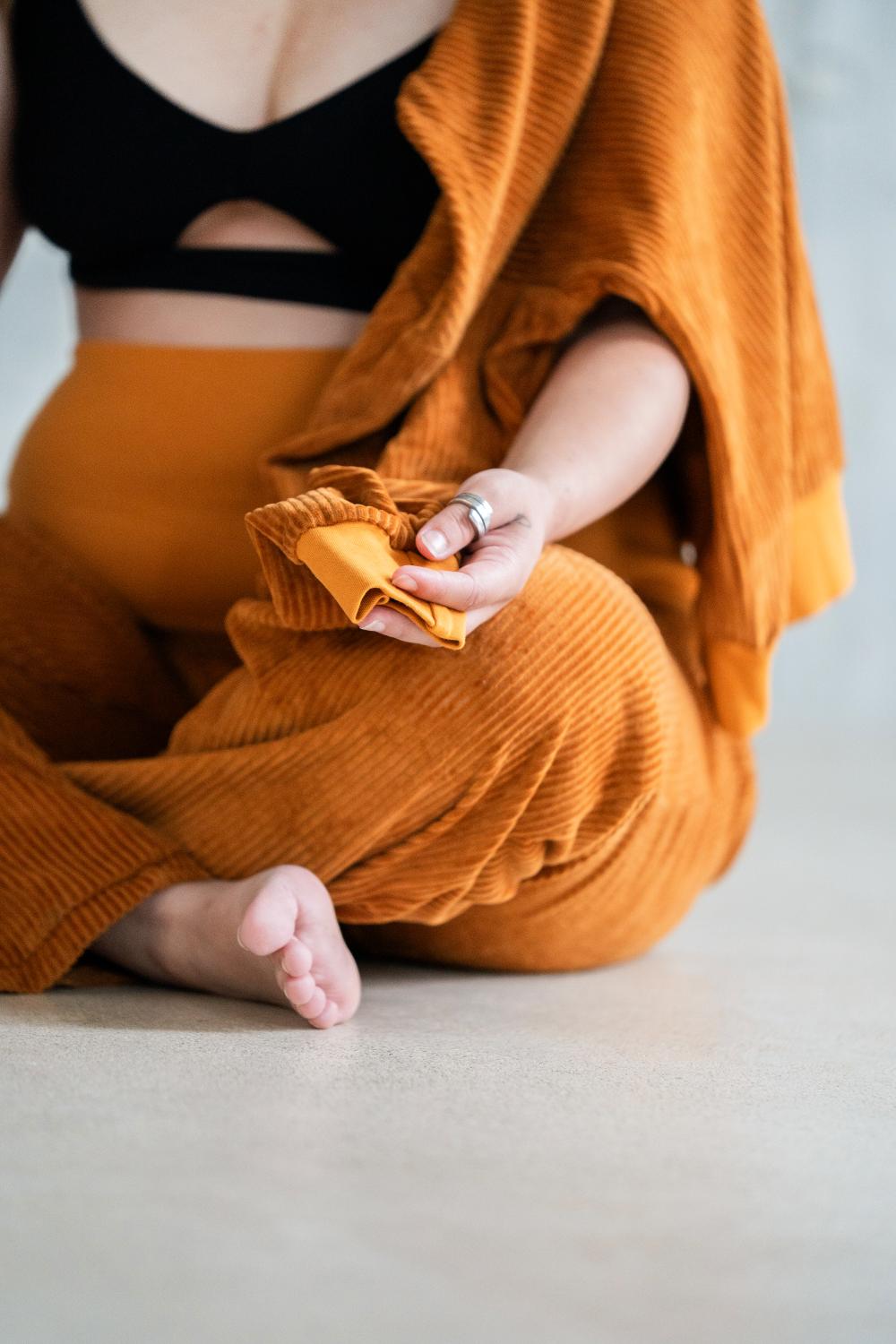 Model sitzt im ockerfarbigen Pyjama auf dem Boden im Schneidersitz.
