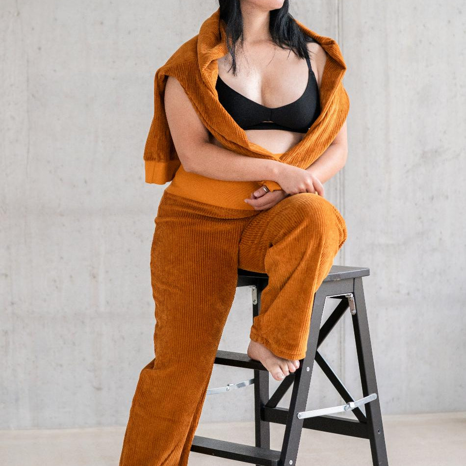 Model trägt Pyjama in ockerfarbigem Cord mit weichen Bündchen, den Pullover hat sie lässig über die Schultern gelegt.