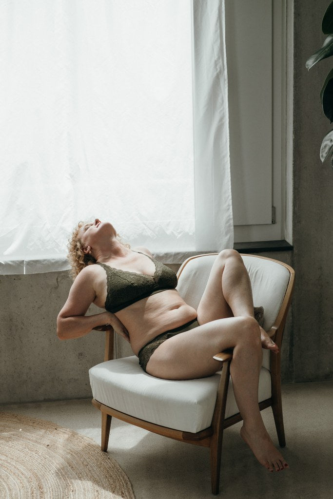 Model trägt das Gisele Set in Olive und sitzt auf einem weissen Sessel. Den Rücken streckt sie über eine Armlehne.