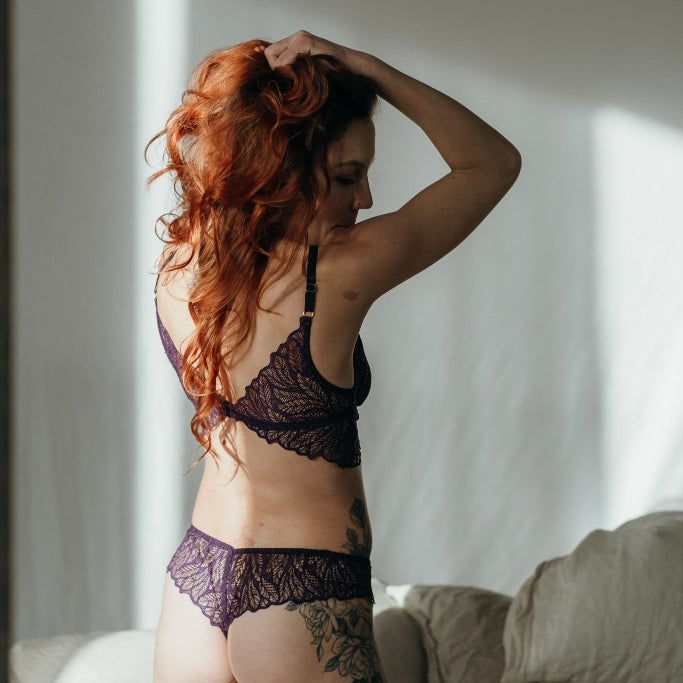 Moodbild von Joanne in Ultraviolet. Model kniet auf dem Bett, den Rücken zur Kamera gewandt und fährt sich mit den Händen durch die Haare. Die Sonne scheint zum Fenster hinein.