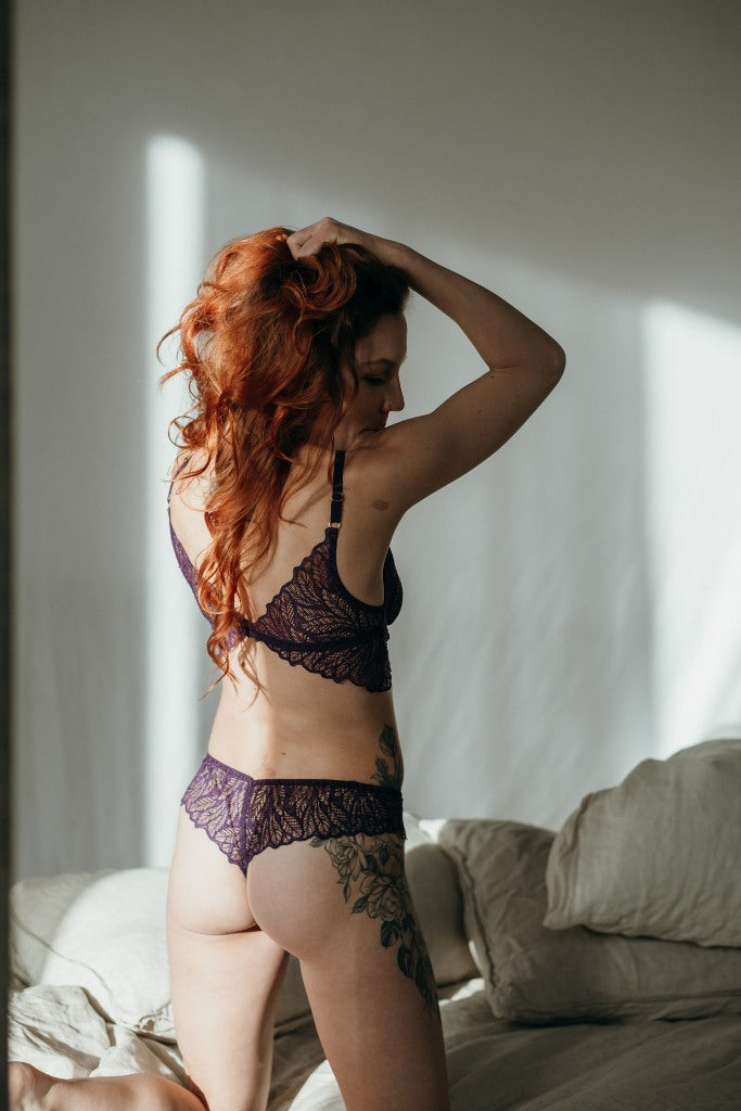 Moodbild von Joanne in Ultraviolet. Model kniet auf dem Bett, den Rücken zur Kamera gewandt und fährt sich mit den Händen durch die Haare. Die Sonne scheint zum Fenster hinein.