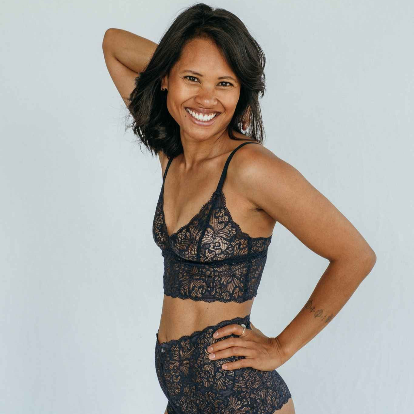 die Frau lacht in die Kamera und präsentiert das Oberteil und den Slip aus Spitze in night blue