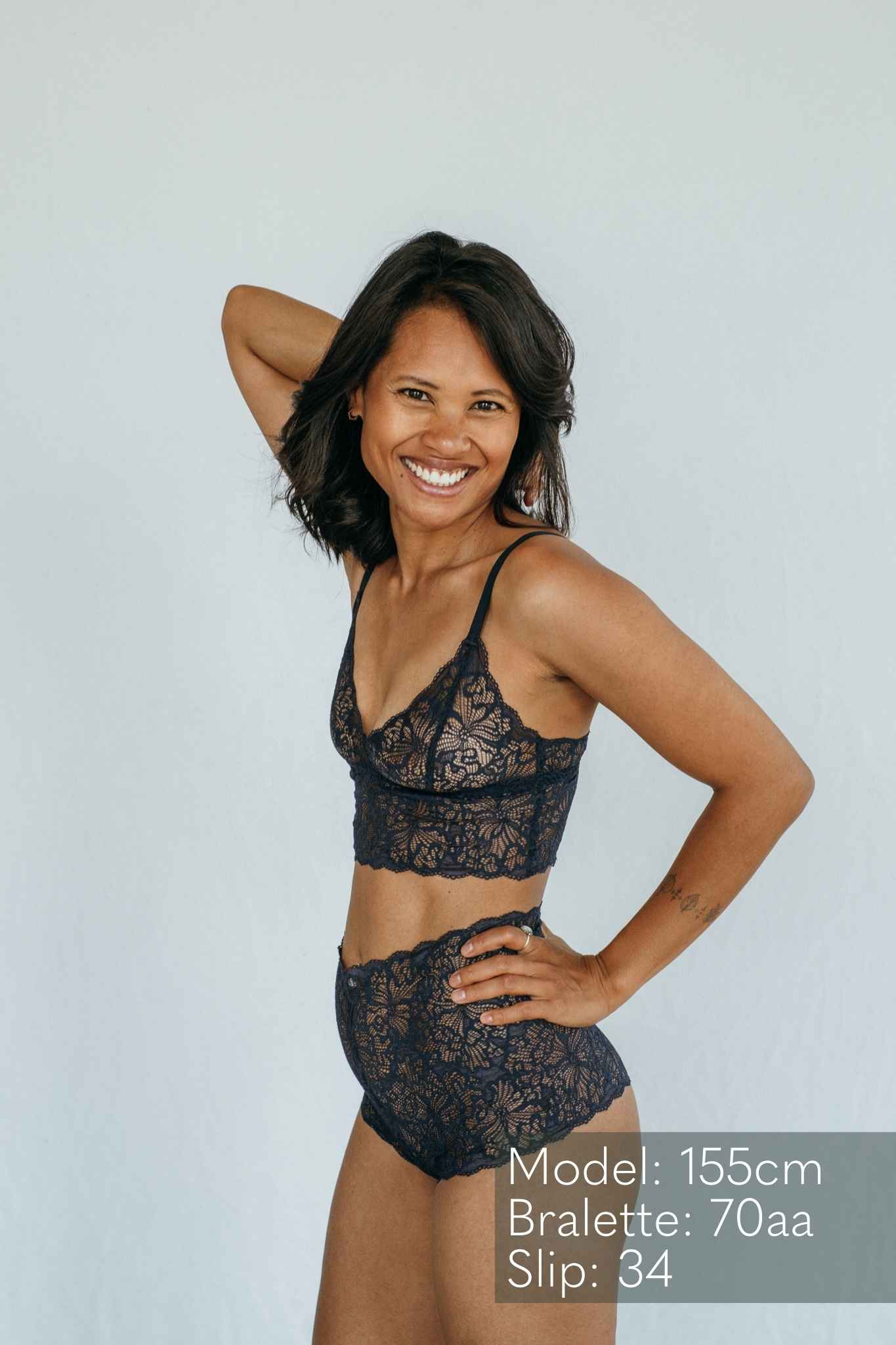 die Frau lacht in die Kamera und präsentiert das Oberteil und den Slip aus Spitze in night blue