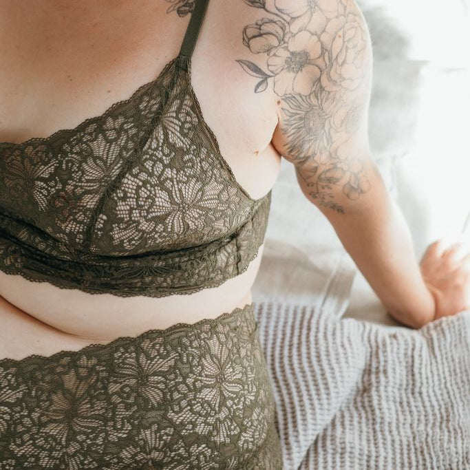 Model trägt Joy Set in der Farbe Olive. Sie sitzt auf dem Bett.