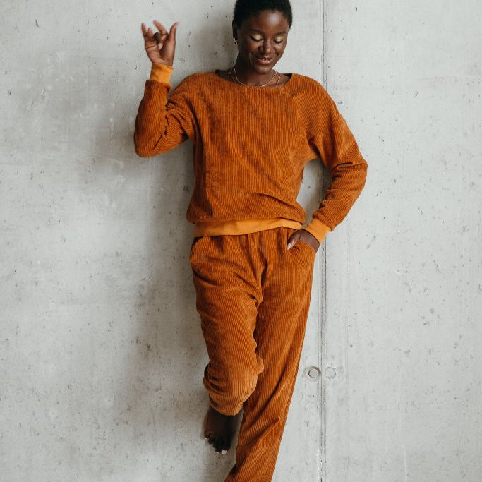 Model trägt Pyjama in ockerfarbigem Cord und lehnt lässig gegen die Wand