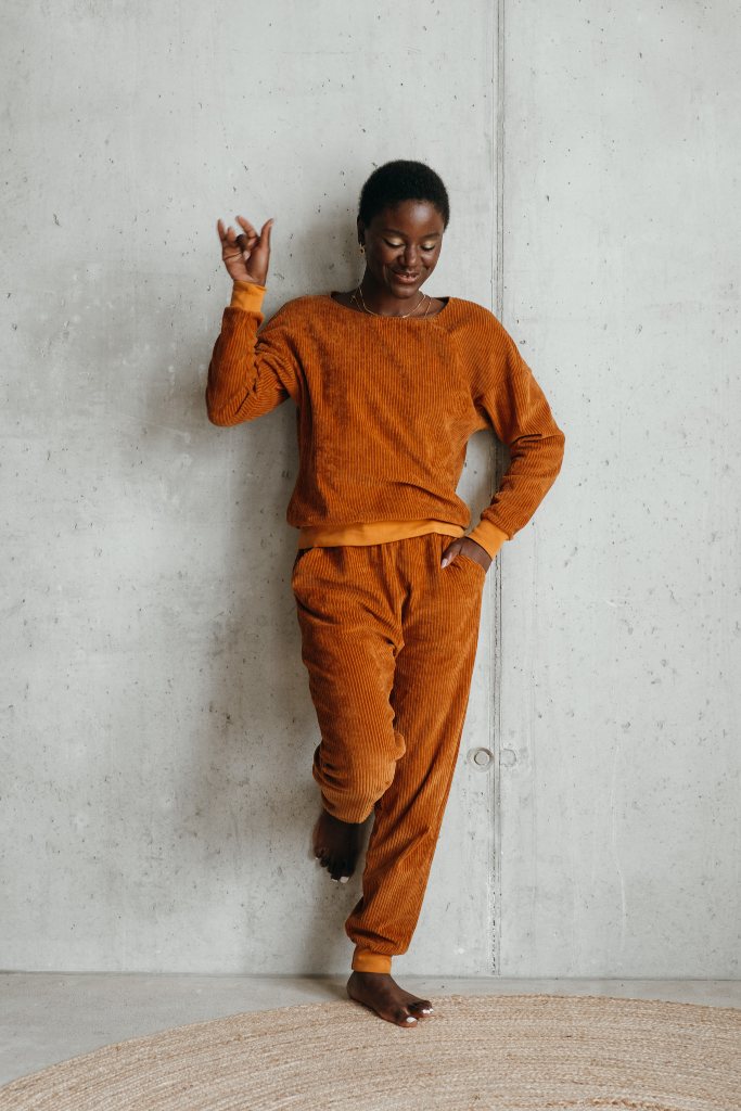 Model trägt Pyjama in ockerfarbigem Cord und lehnt lässig gegen die Wand