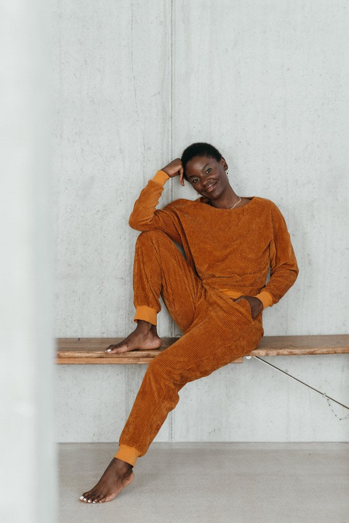 Model sitzt im ockerfarbigen Pyjama auf einer Sitzbank und lächelt direkt in die Kamera