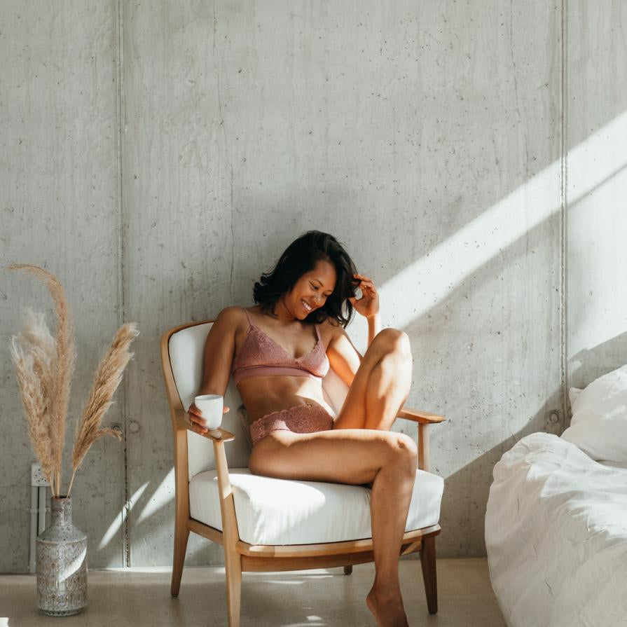 das Model sitzt auf dem Stuhl mit angewinkeltem Bein und trägt dabei schöne Lingerie mit gutem Support