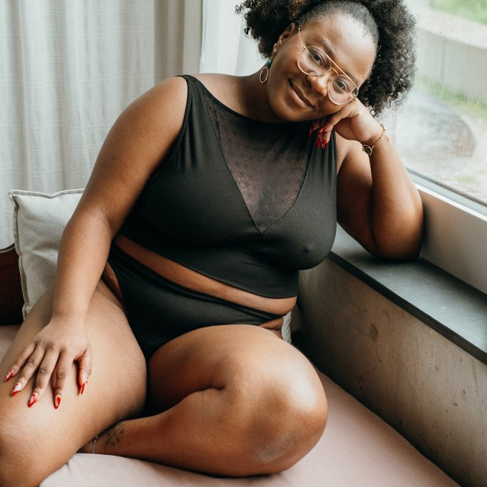 le modèle est assis sur le canapé et pose en tenue Leila en noir