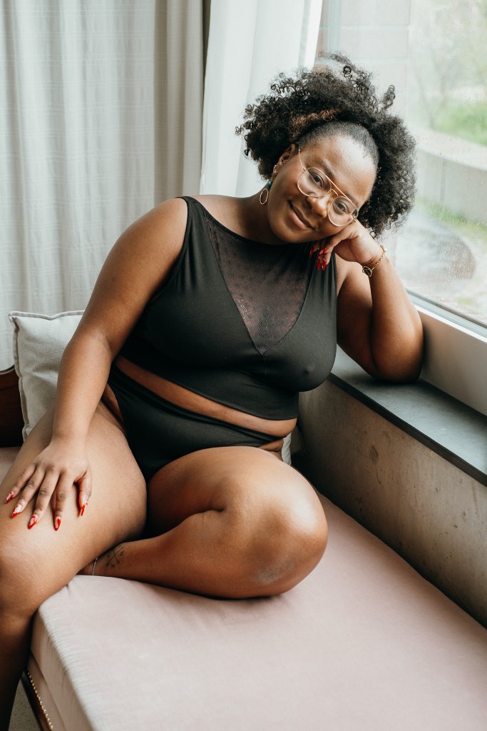 le modèle est assis sur le canapé et pose en tenue Leila en noir