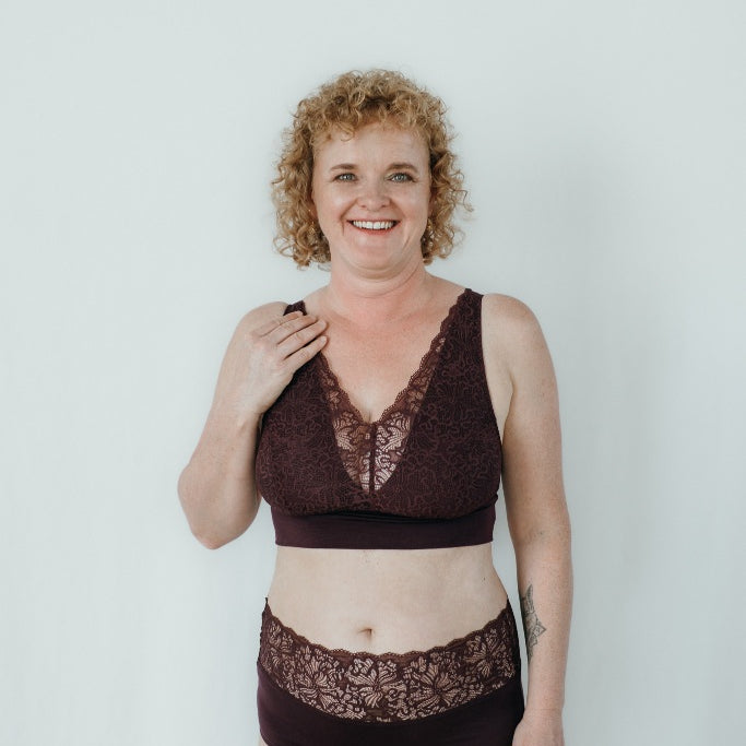 Model trägt das Nelly Set in der Farbe Aubergine. Sie hat blonde, lockige Haare und lächelt in die Kamera.