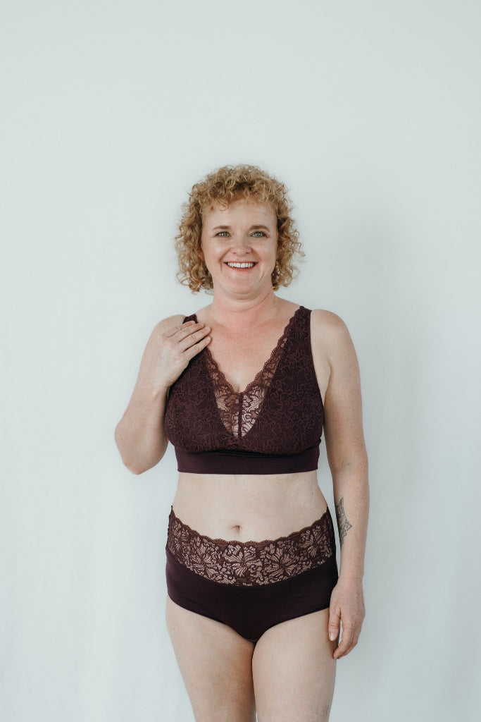 Model trägt das Nelly Set in der Farbe Aubergine. Sie hat blonde, lockige Haare und lächelt in die Kamera.