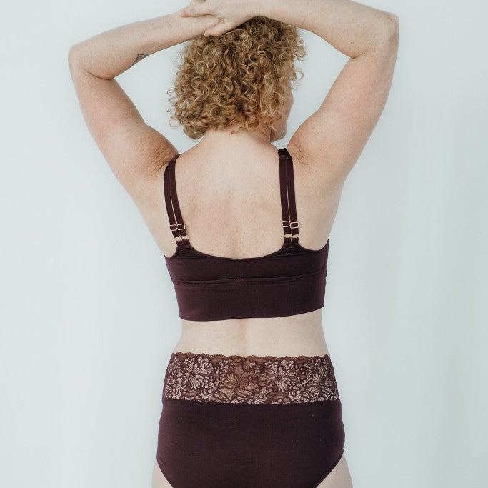 Model trägt das Nelly Set in der Farbe Aubergine, den Rücken hat sie der Kamera zugewandt.