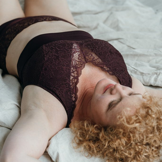 Model liegt im Bett und trägt das Nelly Set in Aubergine. Sie liegt auf dem Rücken und blickt verträumt in die Luft.