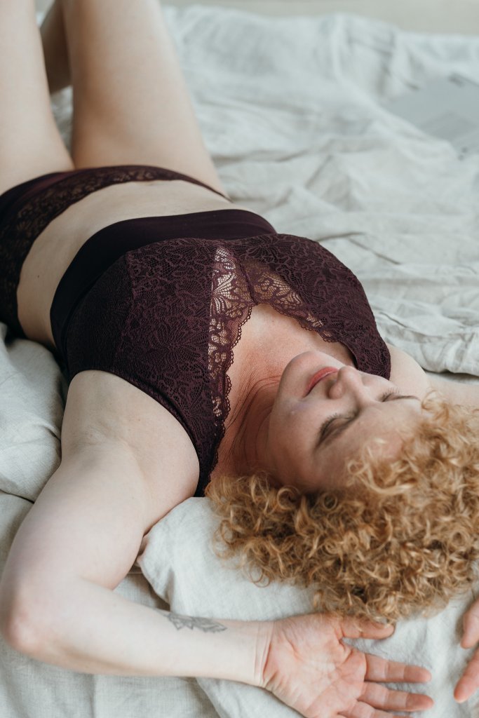 Model liegt im Bett und trägt das Nelly Set in Aubergine. Sie liegt auf dem Rücken und blickt verträumt in die Luft.