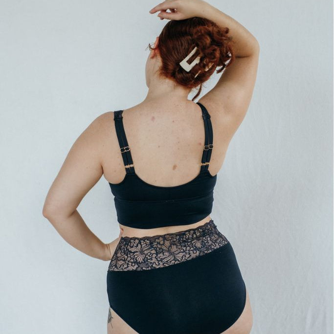 die Frau zeigt sich von hinten und trägt eine Unterhose und ein Büstenhalter in blau aus Spitze und aus Jersey