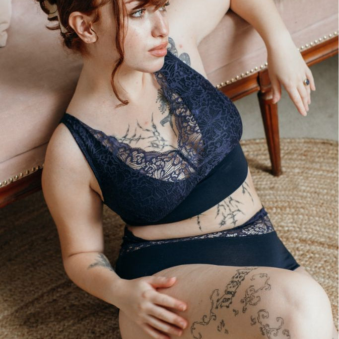 die Frau sitzt auf dem Boden und lehnt sich an. dabei trägt sie Unterwäsche in der Farbe night blue mit doppelten Trägern