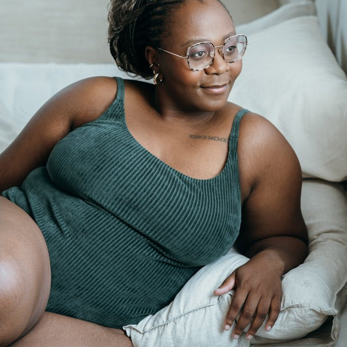 Model trägt jadegrünes Ronja Body und liegt seitwärts auf dem Bett.