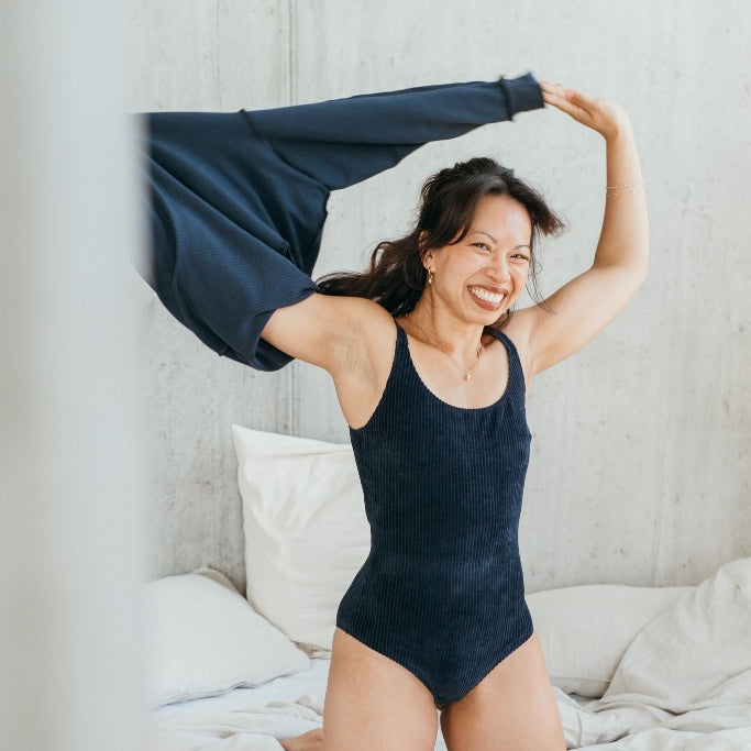 Model trägt das dunkelblaue Ronja Body und zieht sich gerade den dunkelblauen Chloé Pulli aus.