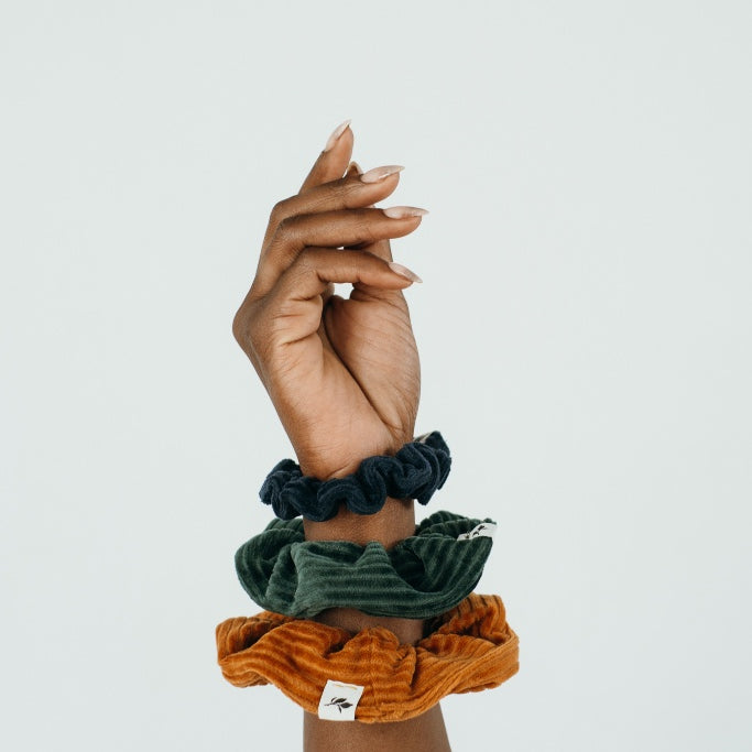 Hand einer Frau, die drei unterschiedliche Scrunchies am Handgelenk trägt.