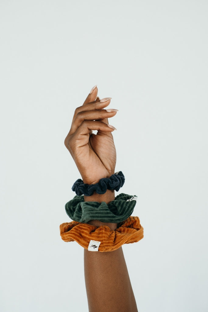 Hand einer Frau, die drei unterschiedliche Scrunchies am Handgelenk trägt.