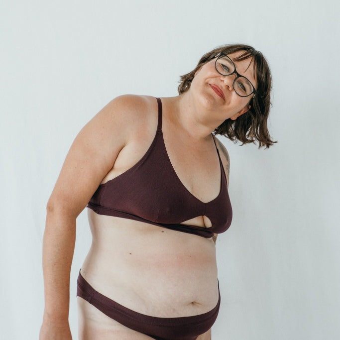 Model trägt das Thea Set in der Farbe Aubergine. Sie steht leicht seitwärts und lächelt in die Kamera.