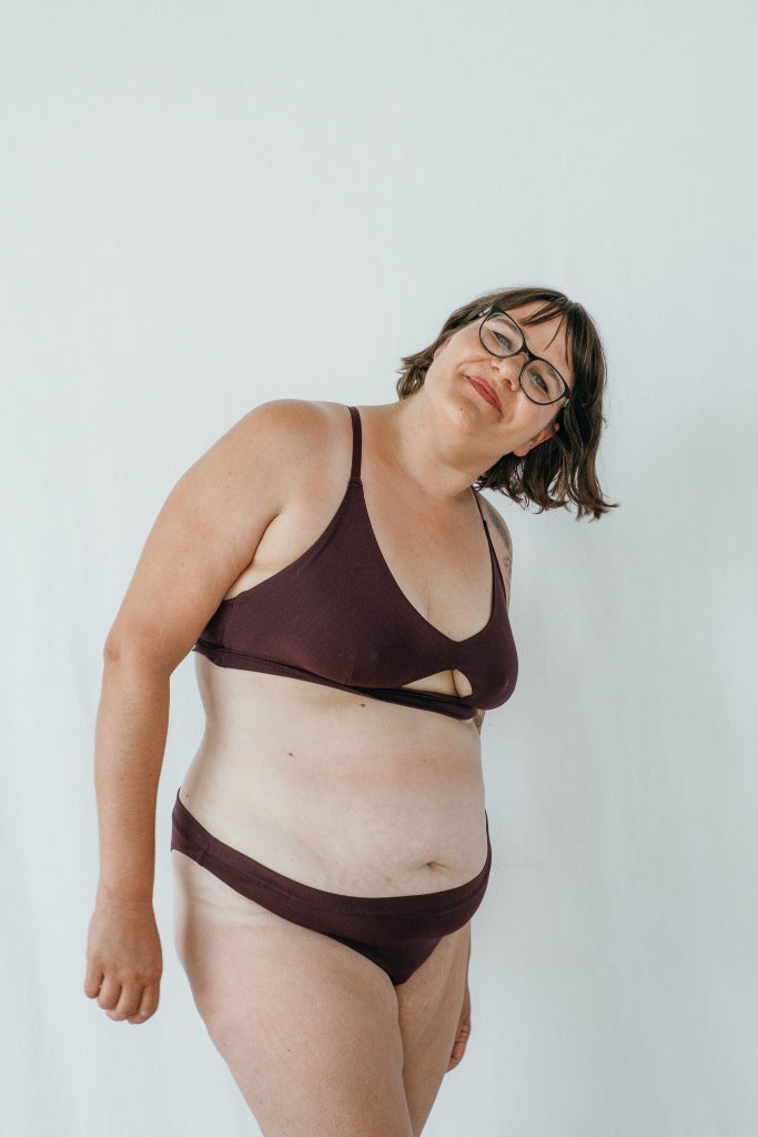 Model trägt das Thea Set in der Farbe Aubergine. Sie steht leicht seitwärts und lächelt in die Kamera.