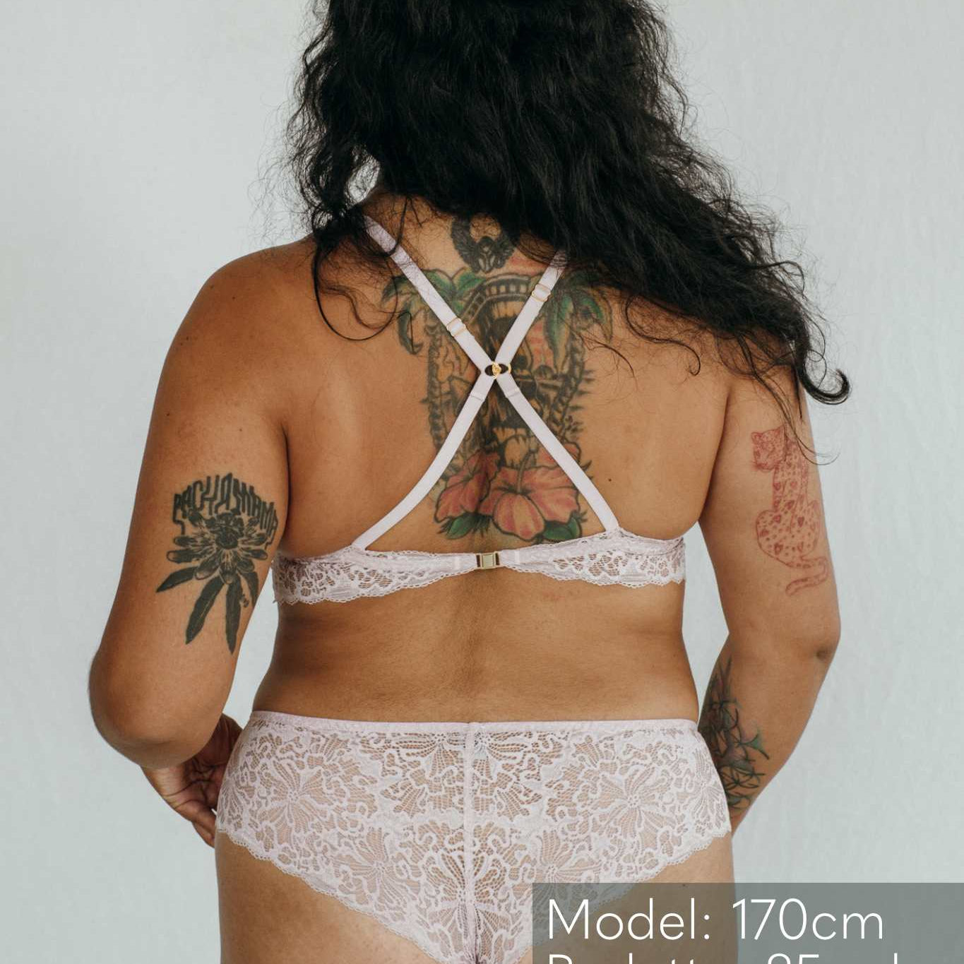 das Model zeigt sich von hinten mit einem Spitzen Slip und einem Bralette, das die Träger kreuzen kann.