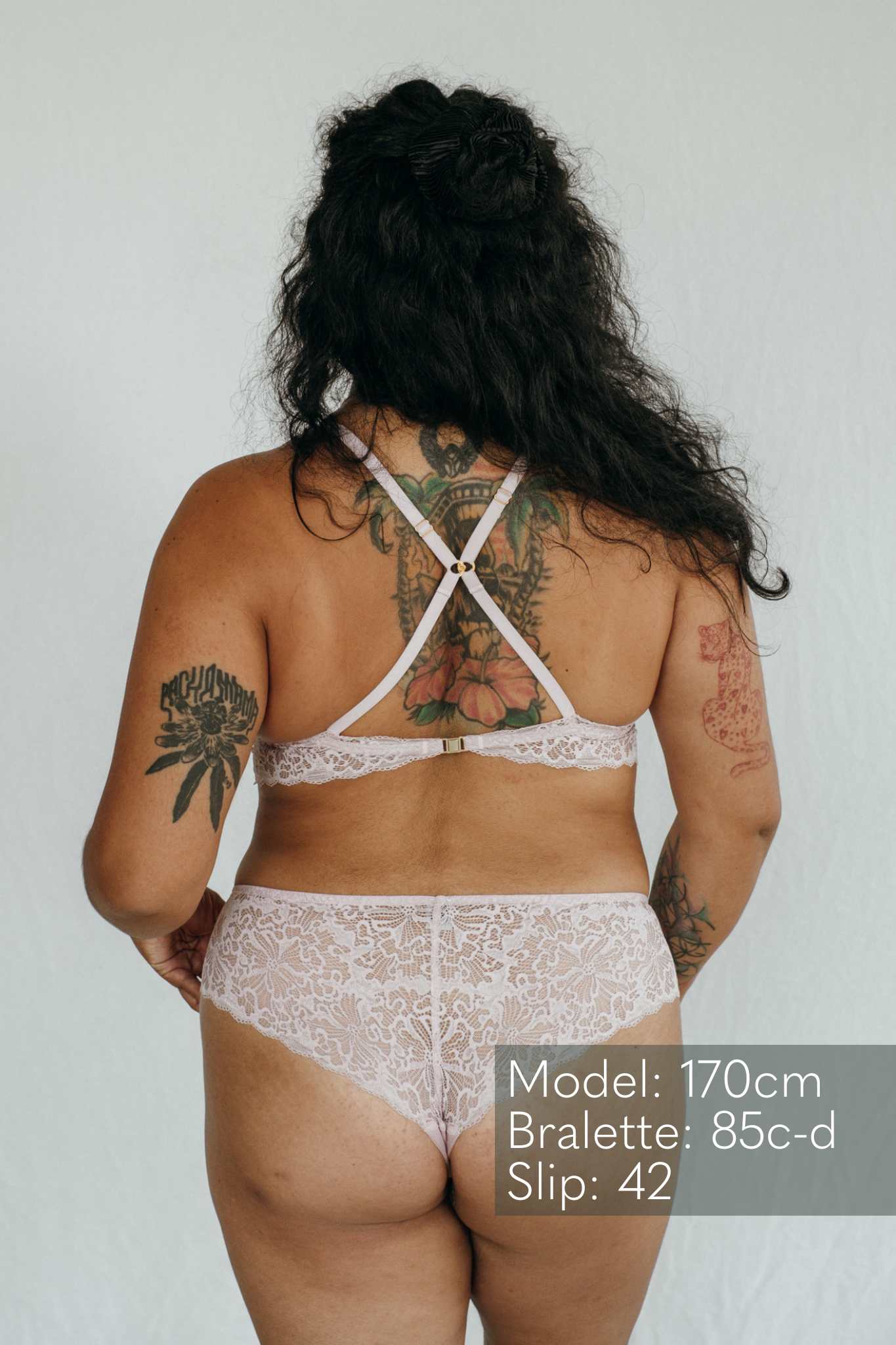 das Model zeigt sich von hinten mit einem Spitzen Slip und einem Bralette, das die Träger kreuzen kann.