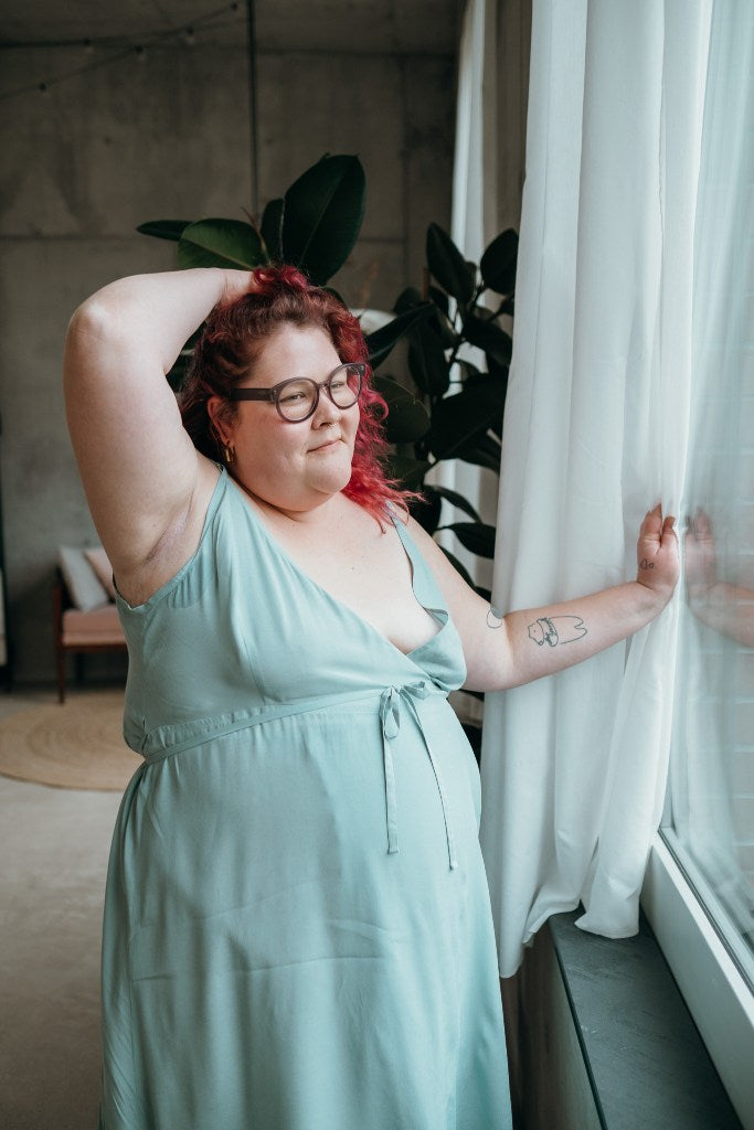 le mannequin aux cheveux roux pose à la fenêtre vêtu de la robe Zia