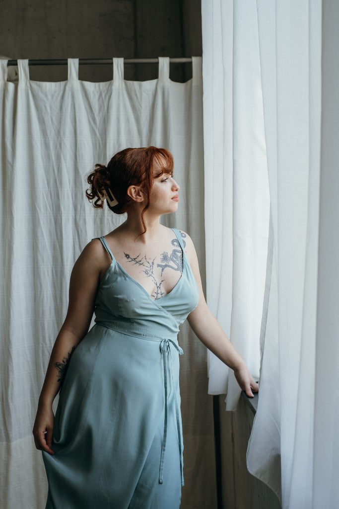 Model trägt das Zia Slipdress in der Farbe Summer Mint. Sie blickt zum Fenster hinaus.