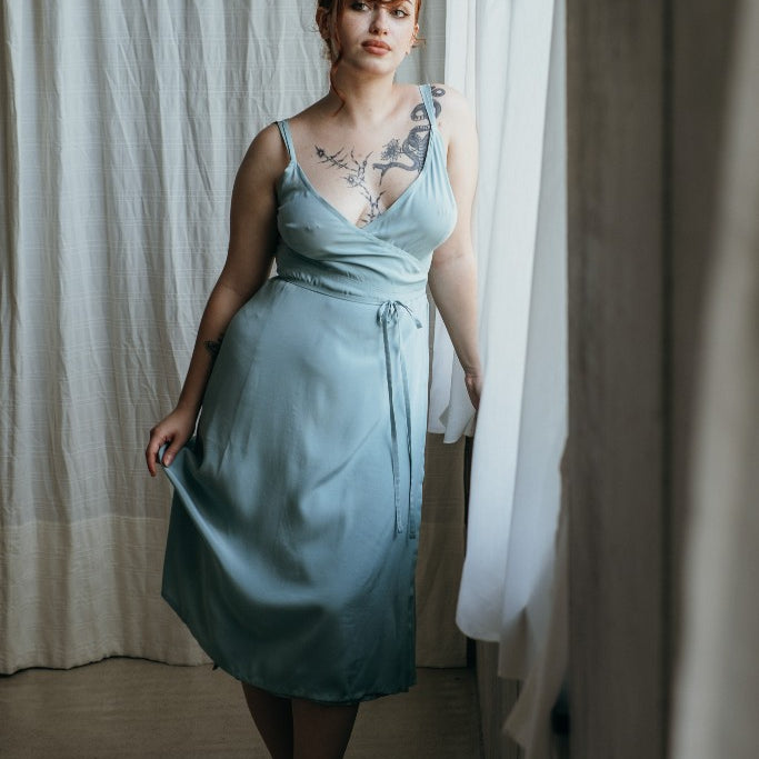 Model trägt das Zia Slipdress in der Farbe Summer Mint. Sie steht am Fenster und blickt in den Raum.
