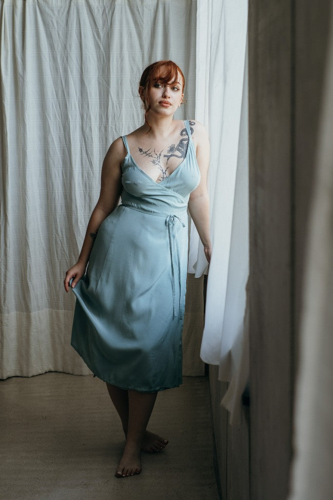 Model trägt das Zia Slipdress in der Farbe Summer Mint. Sie steht am Fenster und blickt in den Raum.
