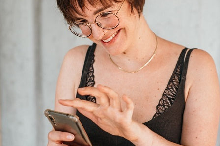 La foto mostra Zippora. È seduta su uno sgabello e scrive sul suo cellulare. Sta sorridendo.