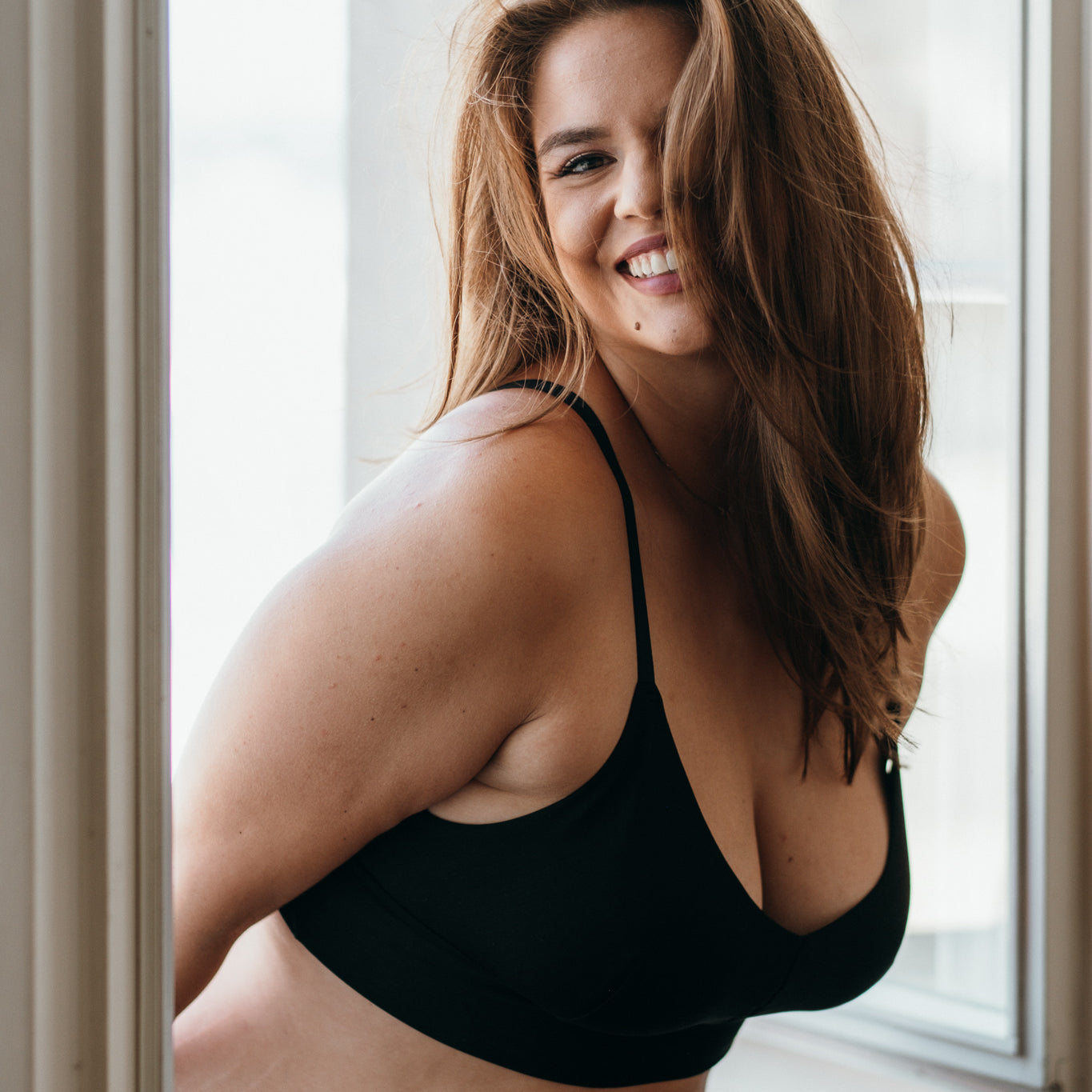 Le mannequin balance ses cheveux et sourit. Elle porte des basiques Bralette et des sous-vêtements en TENCEL™