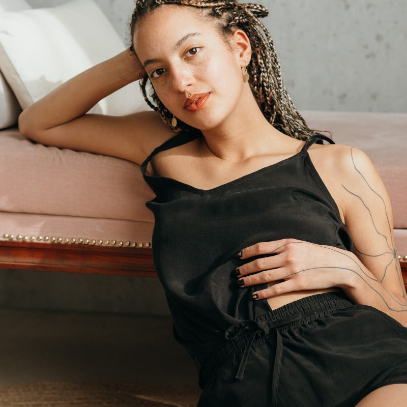 Modèle appuyé contre un canapé, elle porte un haut noir et un pantalon court noir.