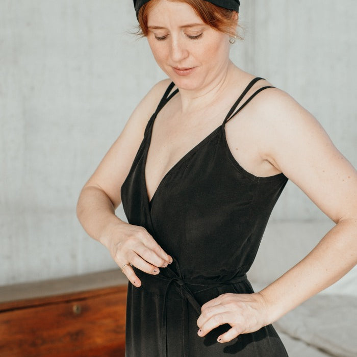 La femme noue avec concentration la robe portefeuille noire en cupro soyeux.