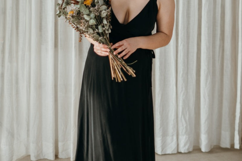 Femme portant une robe portefeuille de thoughts of september et tenant un bouquet de fleurs.