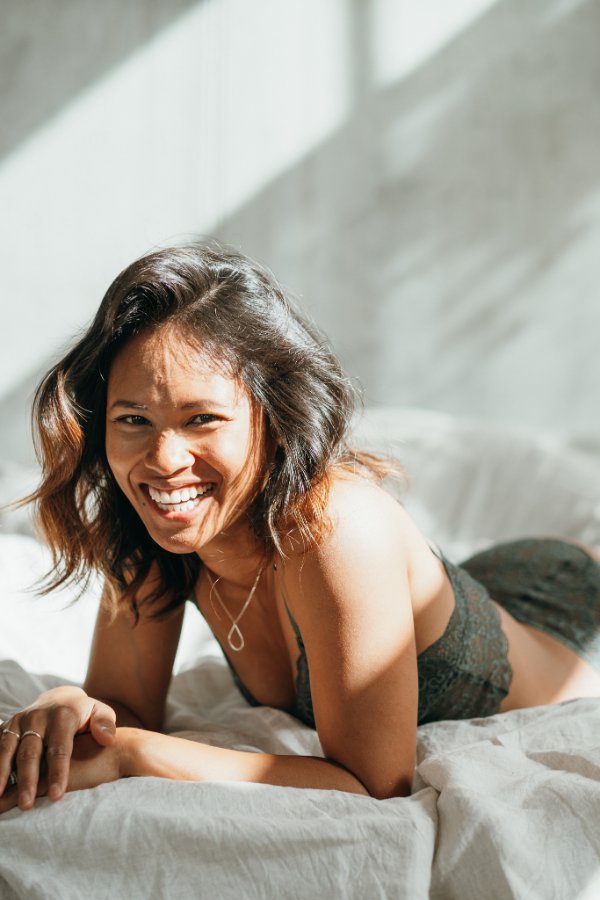 Woman lying on bed and smiling at camera. She is wearing lace underwear.