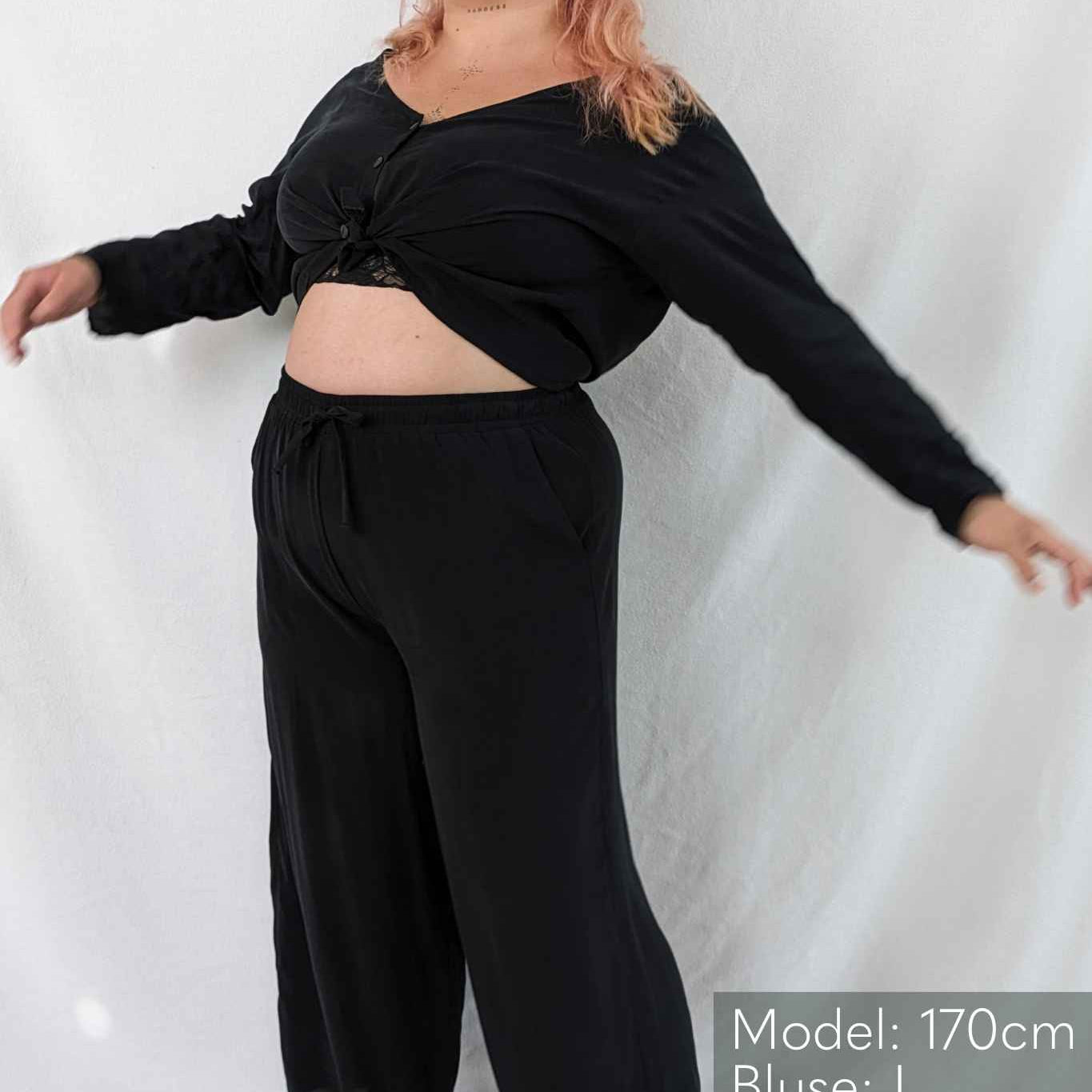 Woman is barefoot and wears black pyjamas and laughs.