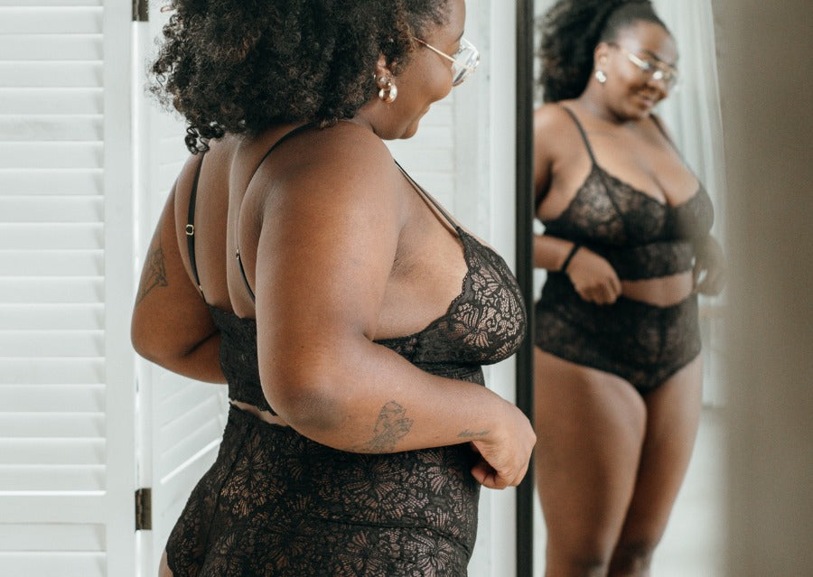 Model in schwarzem Dessous aus Spitze steht vor grossem Spiegel.