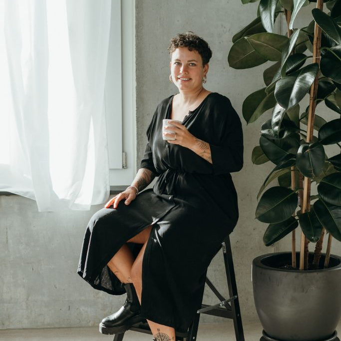 Die Frau sitzt mit einem Kaffee in der Hand und präsentiert sich im schwarzen Morgenmantel.