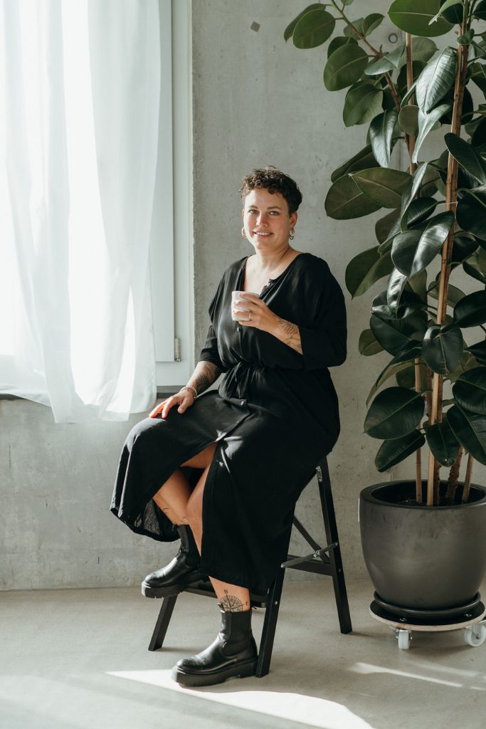 Die Frau sitzt mit einem Kaffee in der Hand und präsentiert sich im schwarzen Morgenmantel.