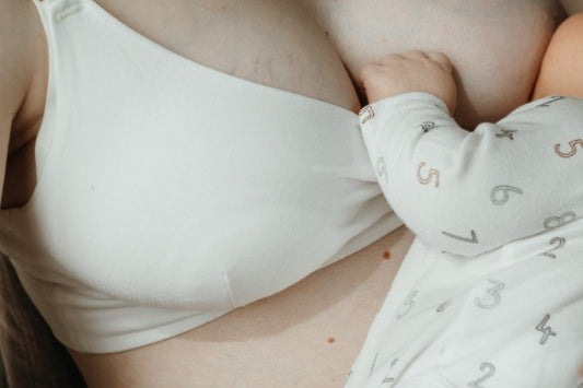 Die Frau stillt ihr Baby und trägt ein weisses Still Bralette