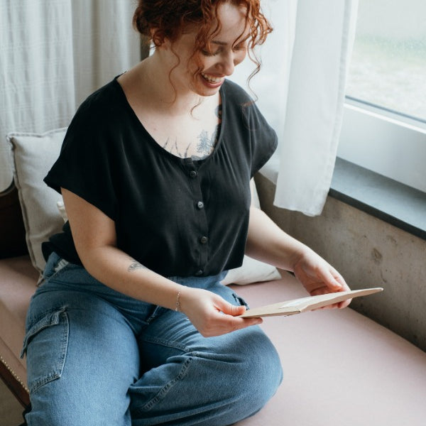 the woman looks at the order while wearing the buttoned-up Noe blouse