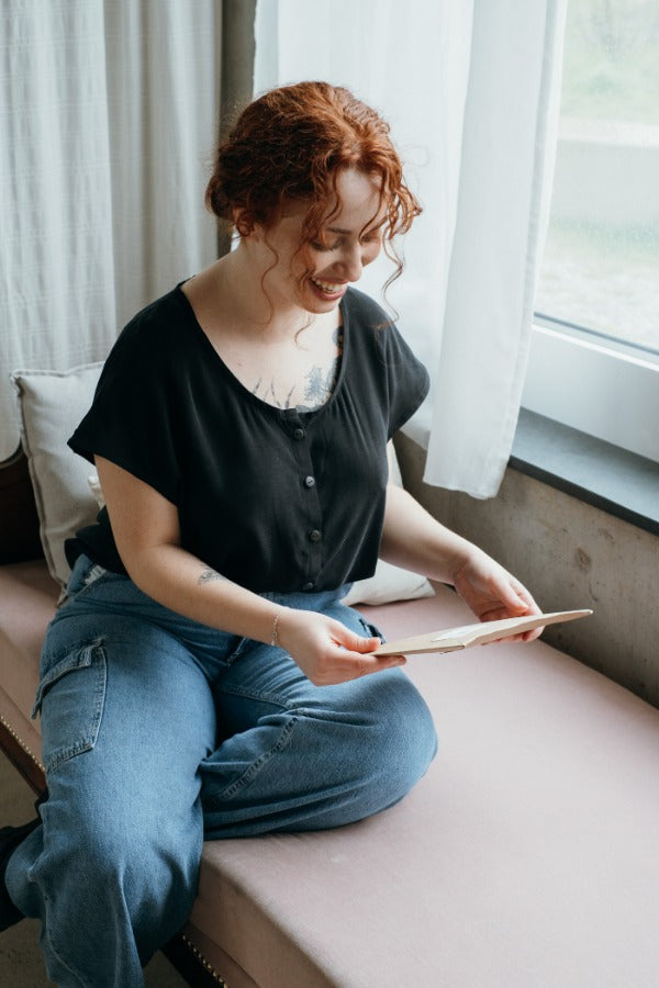 the woman looks at the order while wearing the buttoned-up Noe blouse