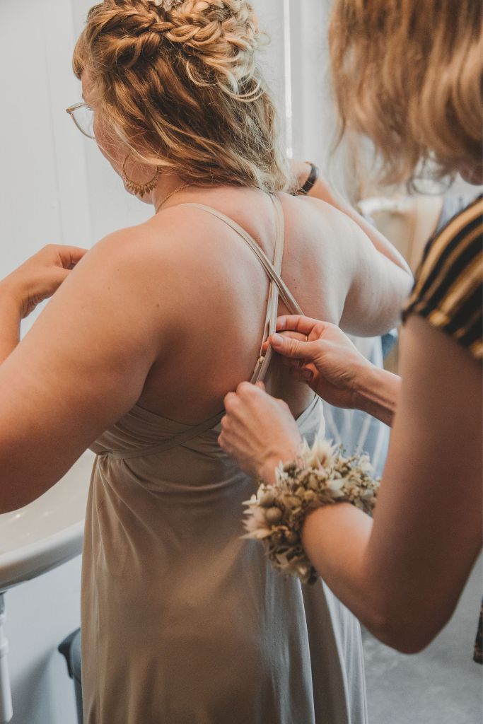 Maid of honor helps the bride put on her Bralette and dress for the wedding.