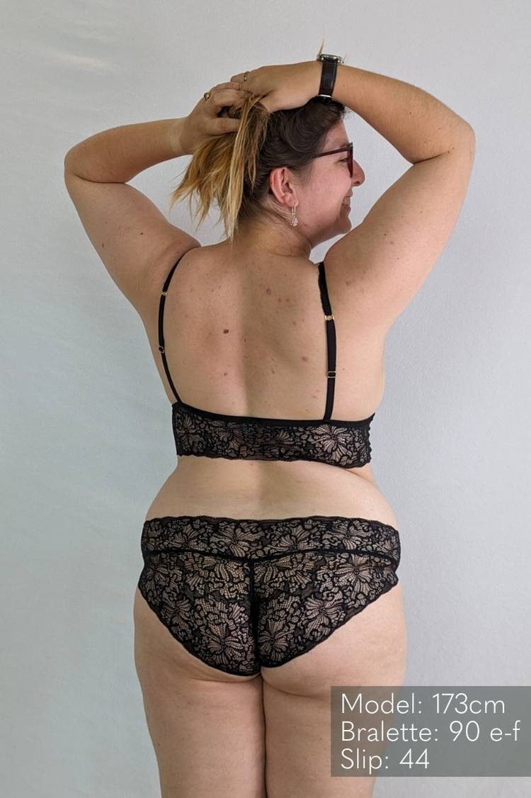 Woman in black lace lingerie holds her hair up.
